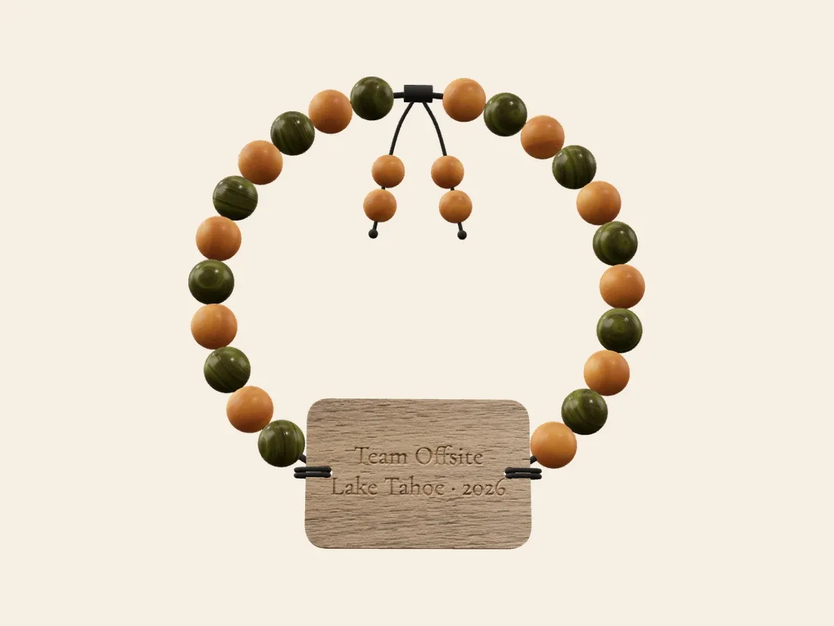 Team offsite bracelet render with alternating green and warm amber beads and a rectangular engraved wood tag